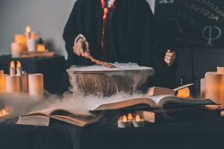 Person in cloak waving wand over cauldron